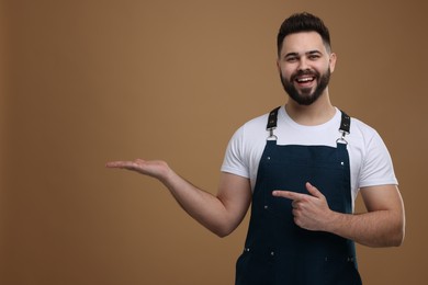 Photo of Smiling man in kitchen apron holding something on brown background. Mockup for design