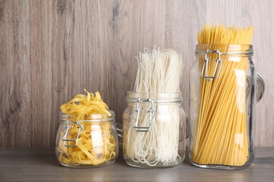 Different types of pasta in glass jars on wooden table