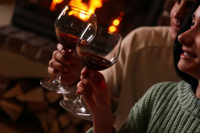 Photo of Lovely couple with glasses of wine near fireplace indoors, closeup. Winter vacation