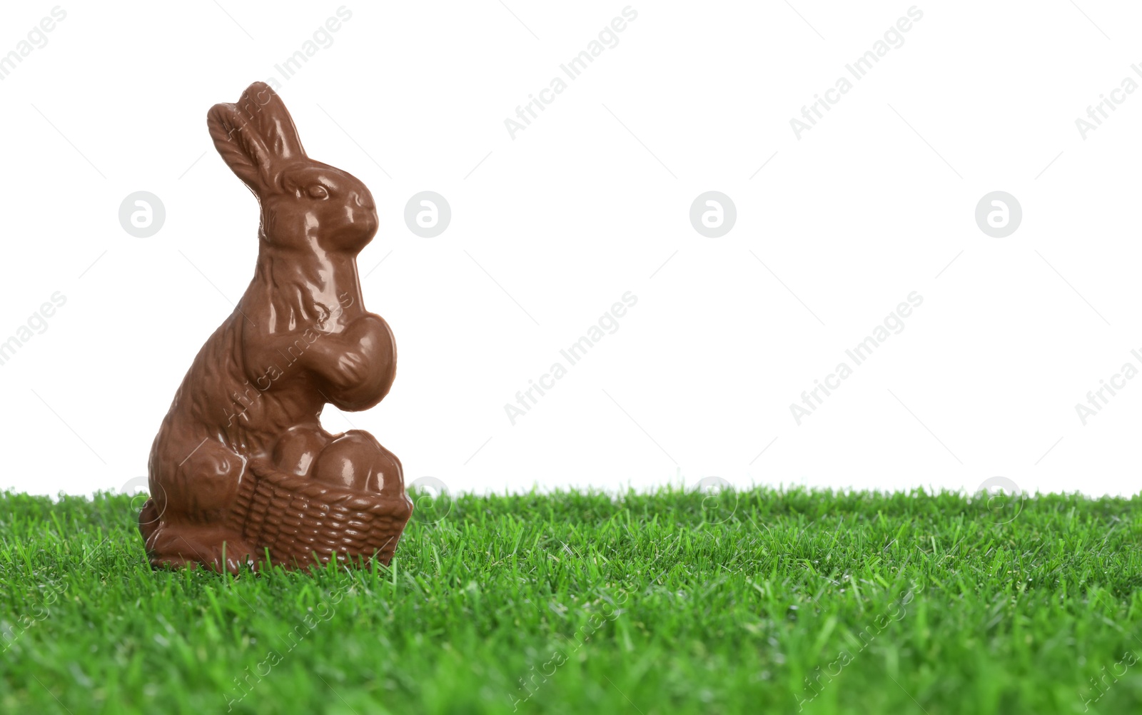 Photo of Chocolate bunny on green grass against white background, space for text. Easter celebration