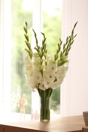 Photo of Vase with beautiful white gladiolus flowers on wooden table in room