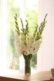 Vase with beautiful white gladiolus flowers on wooden table in room