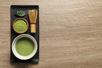 Photo of Cup of fresh matcha tea, bamboo whisk and green powder on wooden table, top view. Space for text