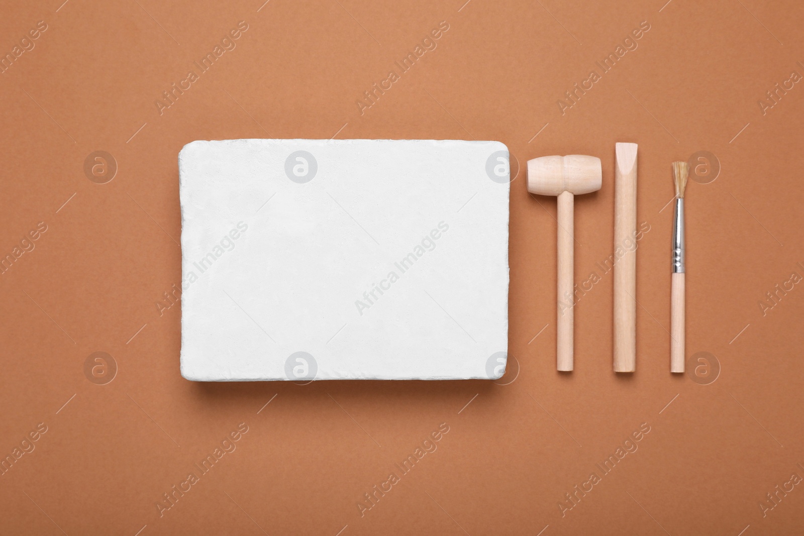 Photo of Educational toy for motor skills development. Excavation kit (plaster, digging tools and brush) on brown background, flat lay