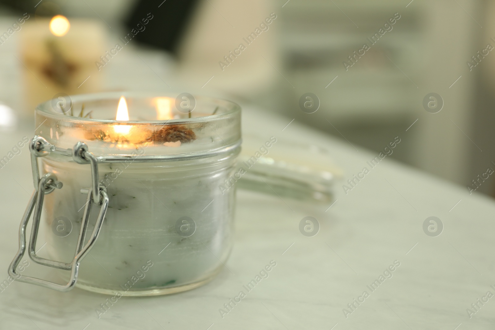 Photo of Burning scented conifer candle on white table indoors. Space for text