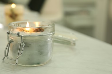 Photo of Burning scented conifer candle on white table indoors. Space for text