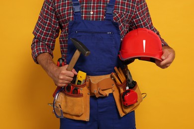 Photo of Professional builder in uniform with hammer and tool belt on yellow background, closeup