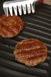 Photo of Taking delicious hamburger patty with tongs from grill pan