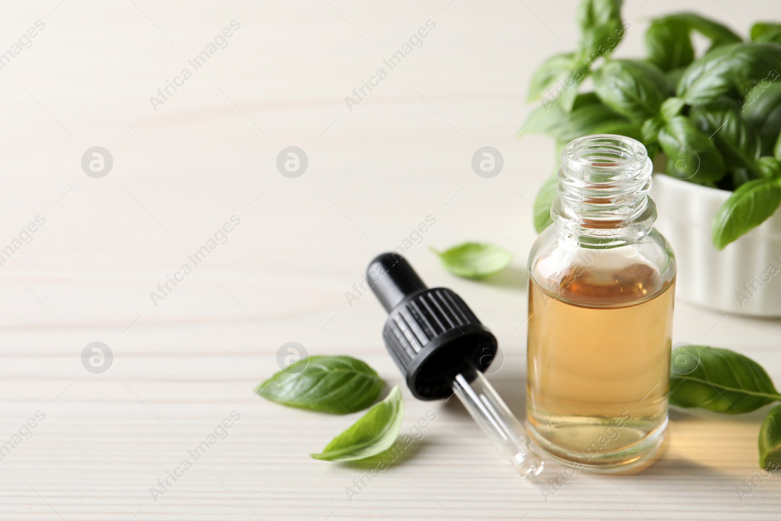 Photo of Glass bottle of basil essential oil and leaves on white wooden table. Space for text