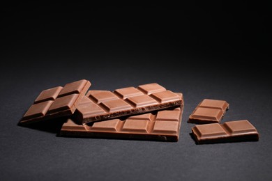 Photo of Pieces of delicious milk chocolate bars on black background