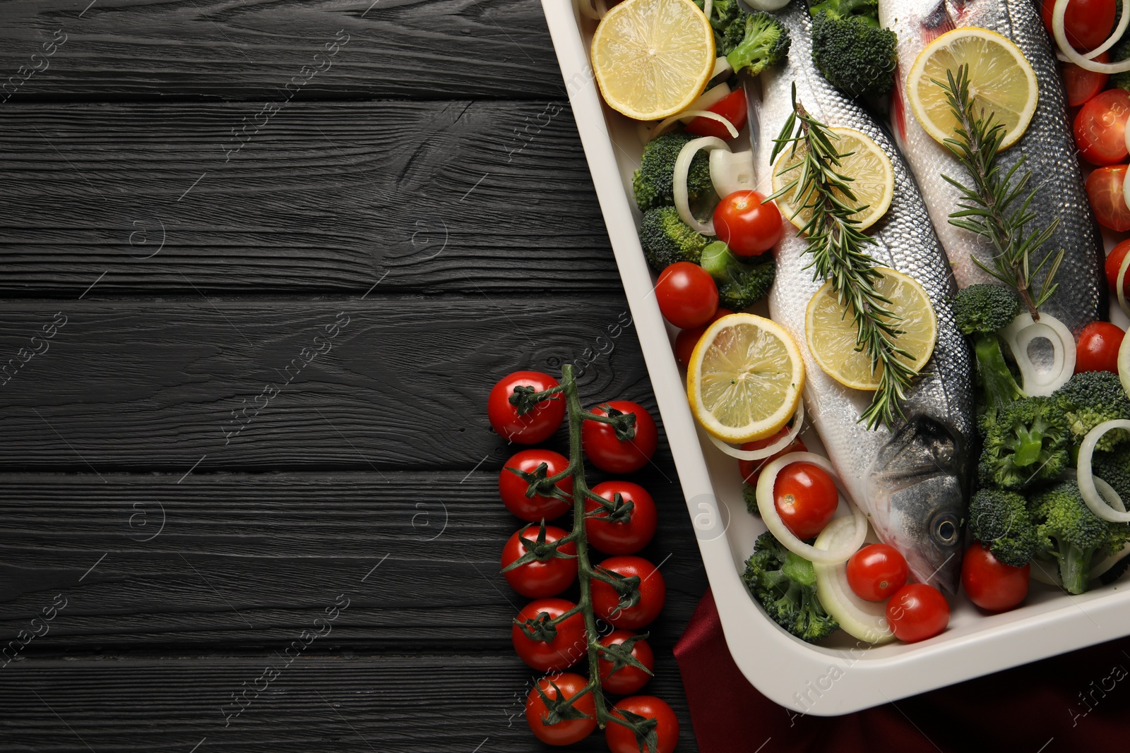 Photo of Raw fish with lemon in baking dish and vegetables on black wooden table, flat lay. Space for text