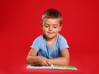 Cute little boy reading book on red background