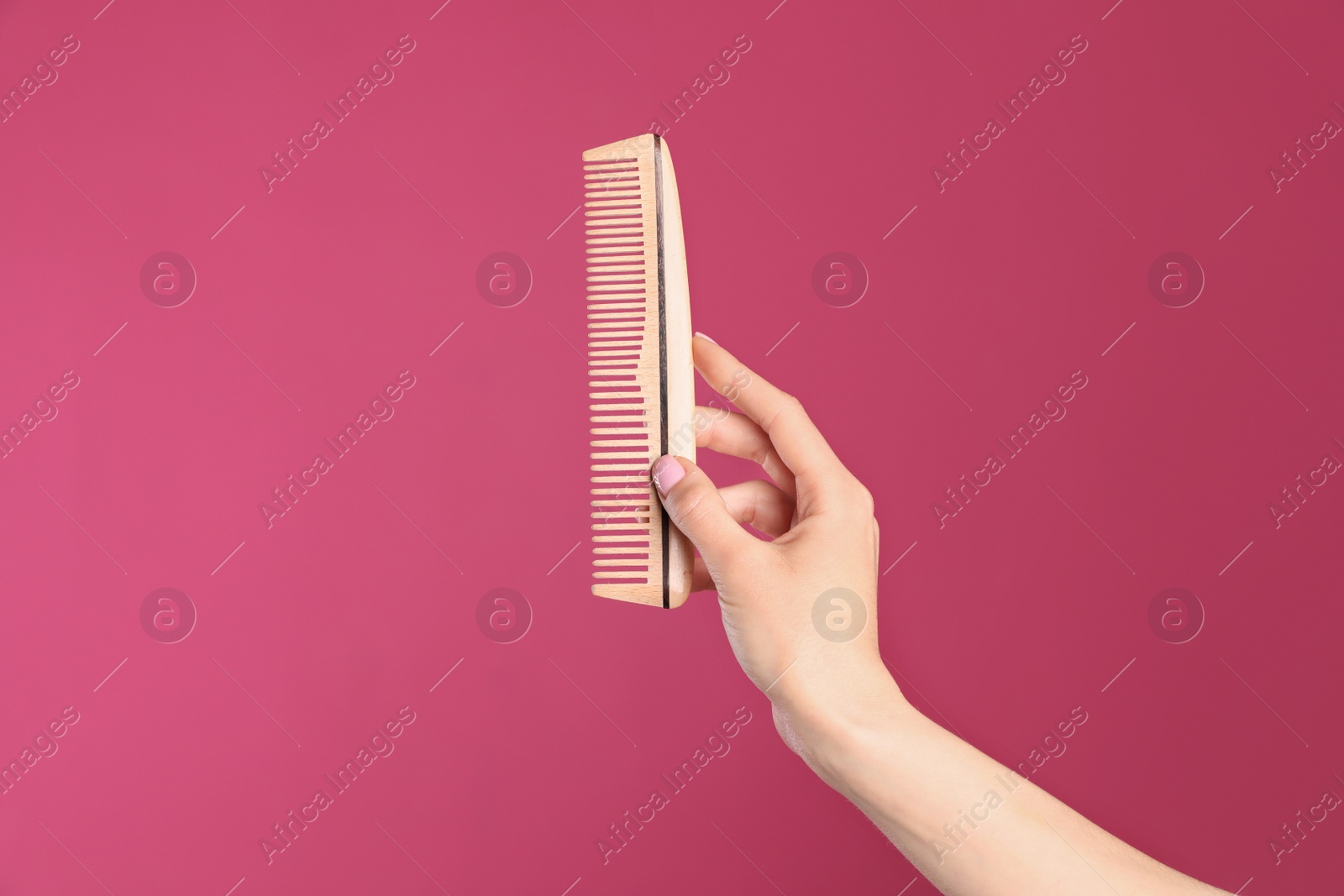 Photo of Woman holding wooden hair comb against crimson background, closeup. Space for text