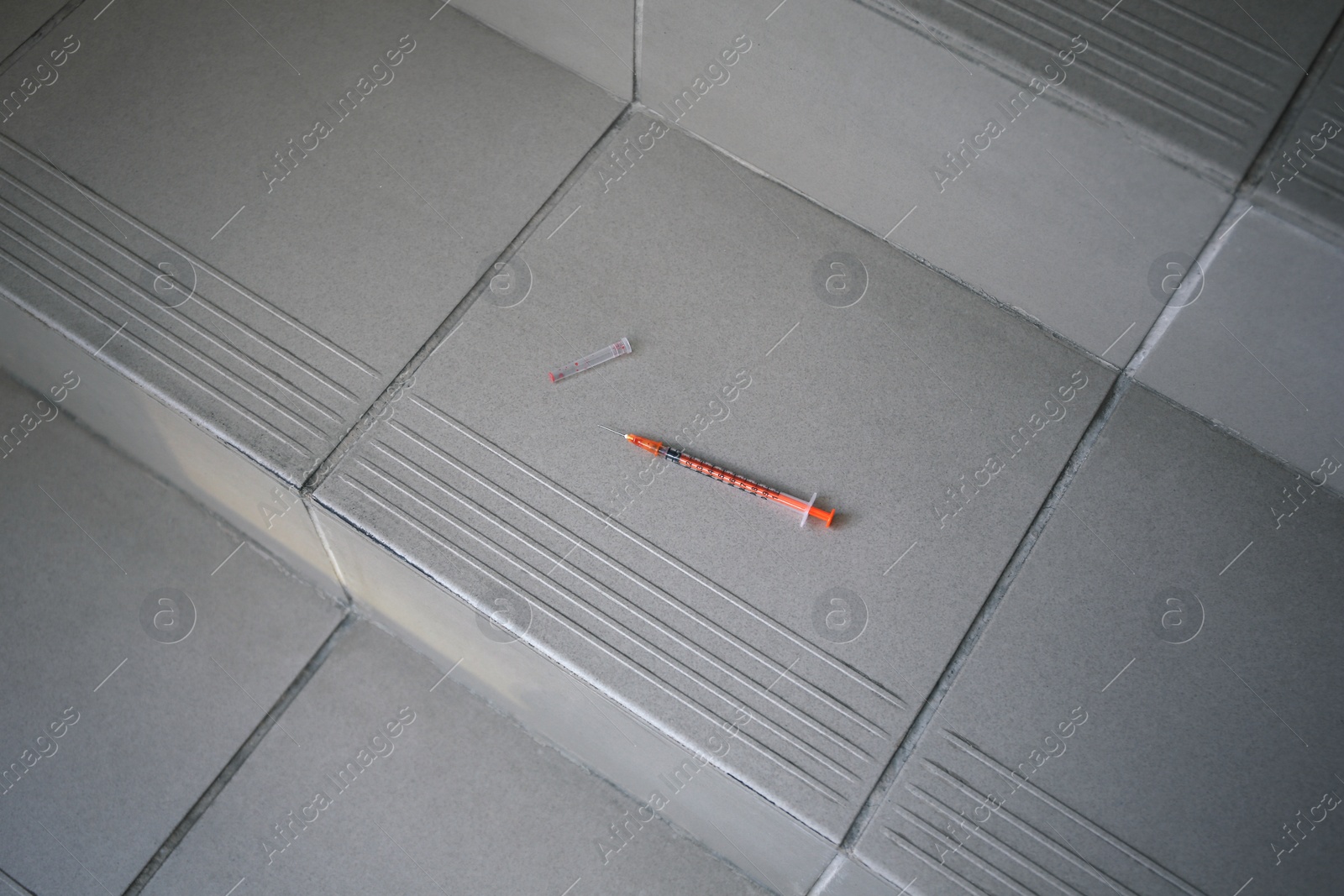 Photo of Disposable syringe with needle on tiled stairs indoors. Space for text