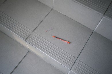 Disposable syringe with needle on tiled stairs indoors. Space for text