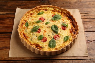 Photo of Delicious quiche with cheese, tomatoes and basil on wooden table