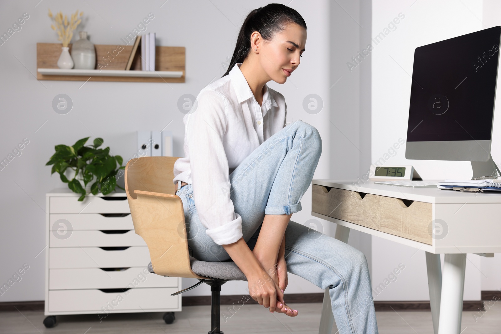 Photo of Young woman rubbing sore foot in office