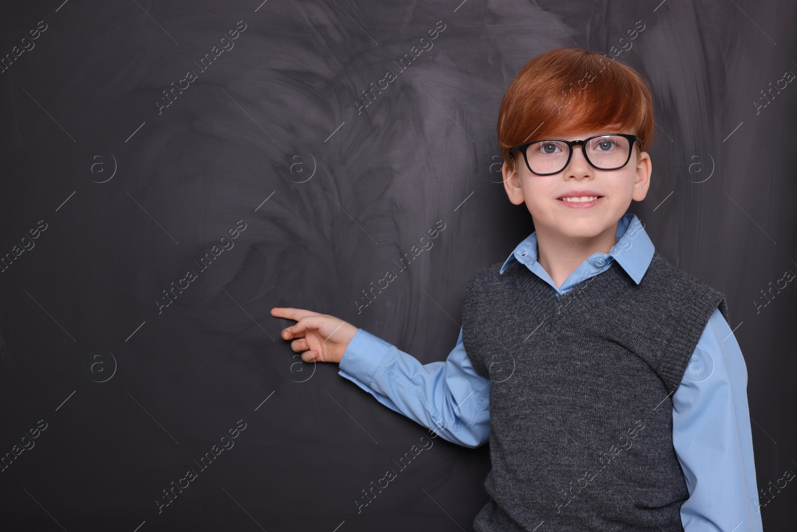 Photo of Smiling schoolboy pointing at something on blackboard. Space for text