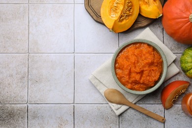 Photo of Bowl of delicious pumpkin jam and fresh pumpkins on tiled surface, flat lay. Space for text