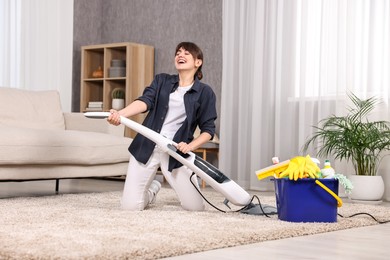 Photo of Happy young housewife having fun while cleaning carpet at home