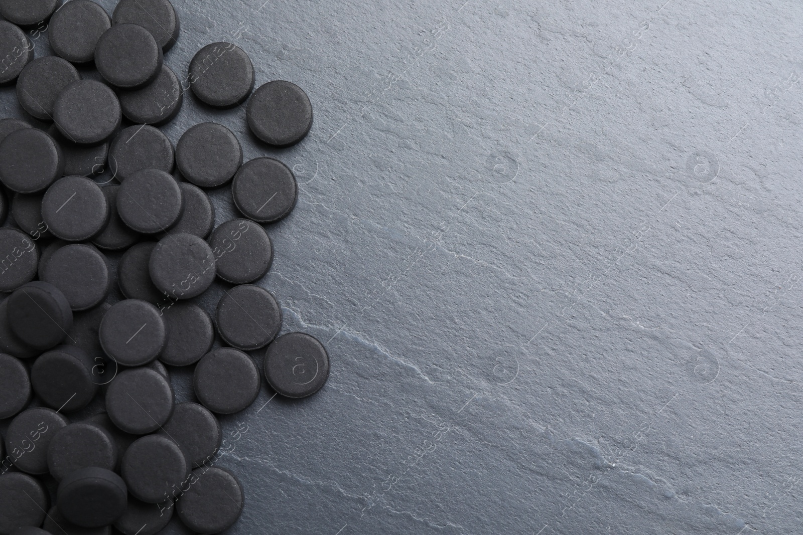 Photo of Pile of activated charcoal pills on black table, flat lay with space for text. Potent sorbent