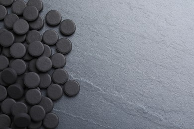 Photo of Pile of activated charcoal pills on black table, flat lay with space for text. Potent sorbent
