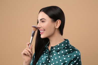 Happy woman with makeup brush on light brown background