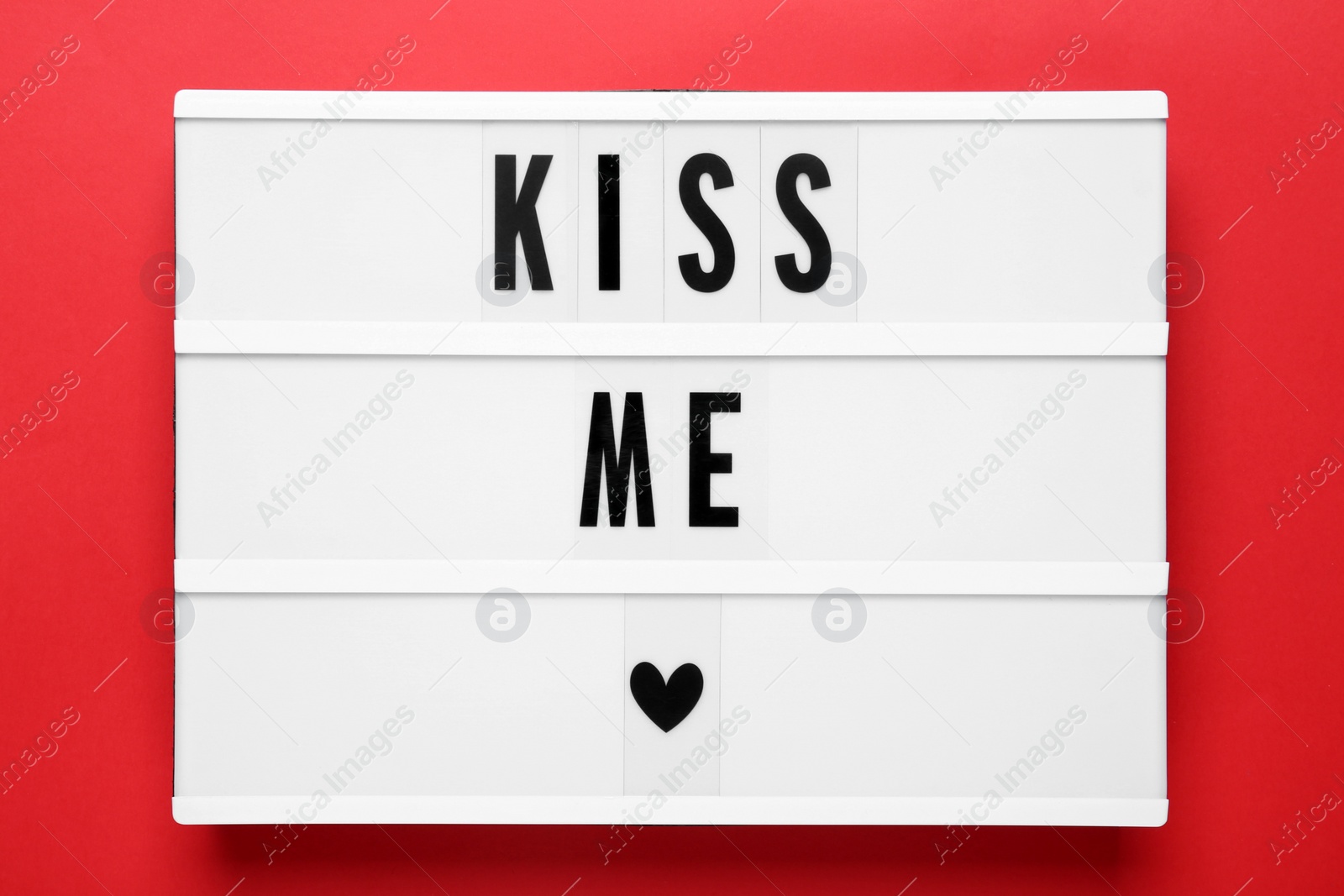 Photo of Light box with phrase Kiss Me on red background, top view