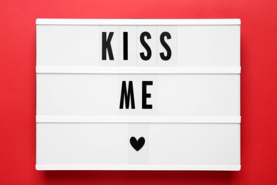 Photo of Light box with phrase Kiss Me on red background, top view