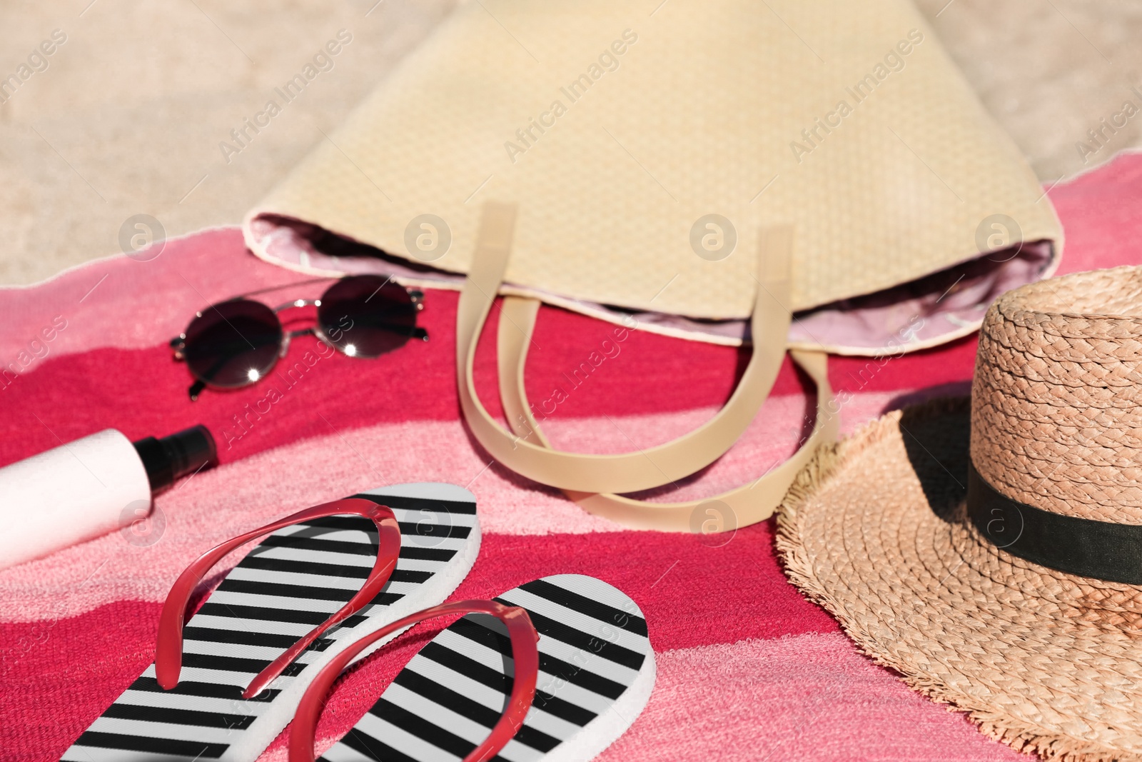 Photo of Striped flip flops, bag and other beach items on sand, closeup