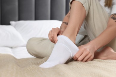 Photo of Woman putting on white socks in bedroom, closeup