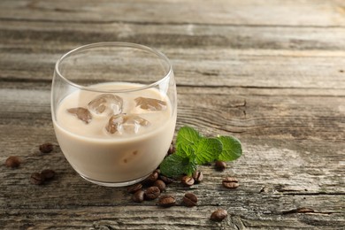 Photo of Coffee cream liqueur in glass, mint and beans on wooden table, space for text
