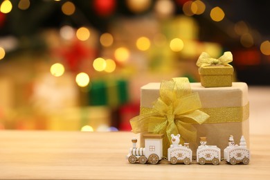 Beautiful gift boxes with toy train on wooden table against blurred festive lights, space for tex. Christmas celebration