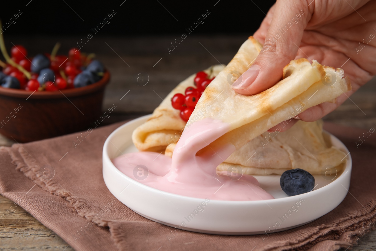 Photo of Woman eating delicious crepe with natural yogurt, blueberries and red currants at wooden table, closeup. Space for text