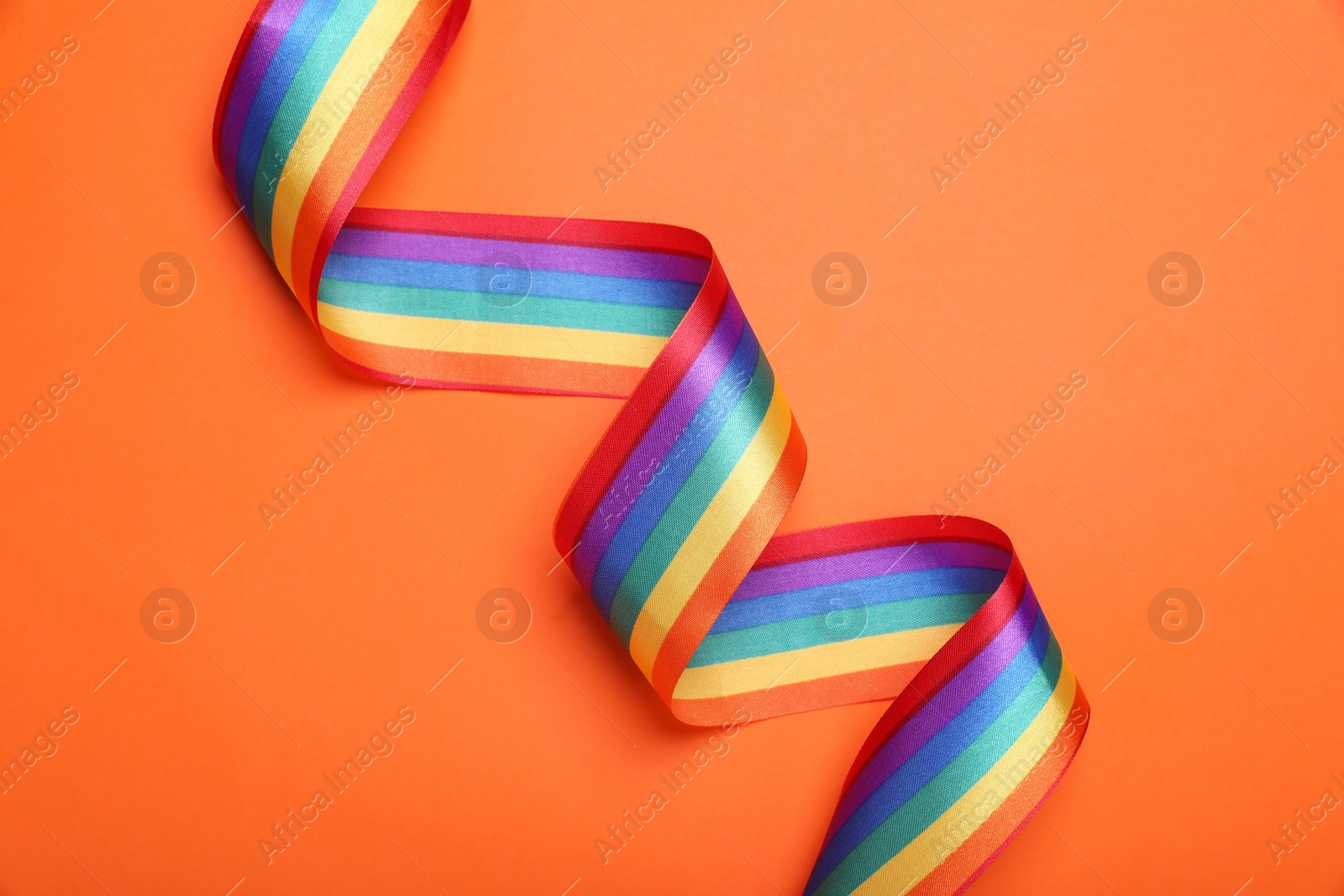 Photo of Rainbow ribbon on orange background, top view. LGBT pride