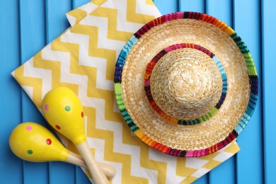 Mexican sombrero hat, towel and maracas on blue wooden surface, top view