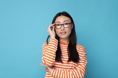 Portrait of happy woman in glasses on light blue background