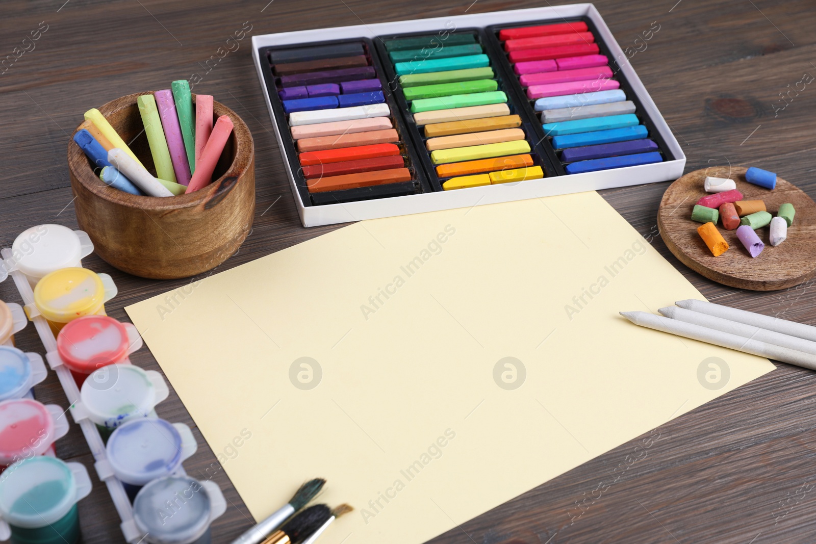 Photo of Blank sheet of paper, colorful chalk pastels and other drawing tools on wooden table. Modern artist's workplace