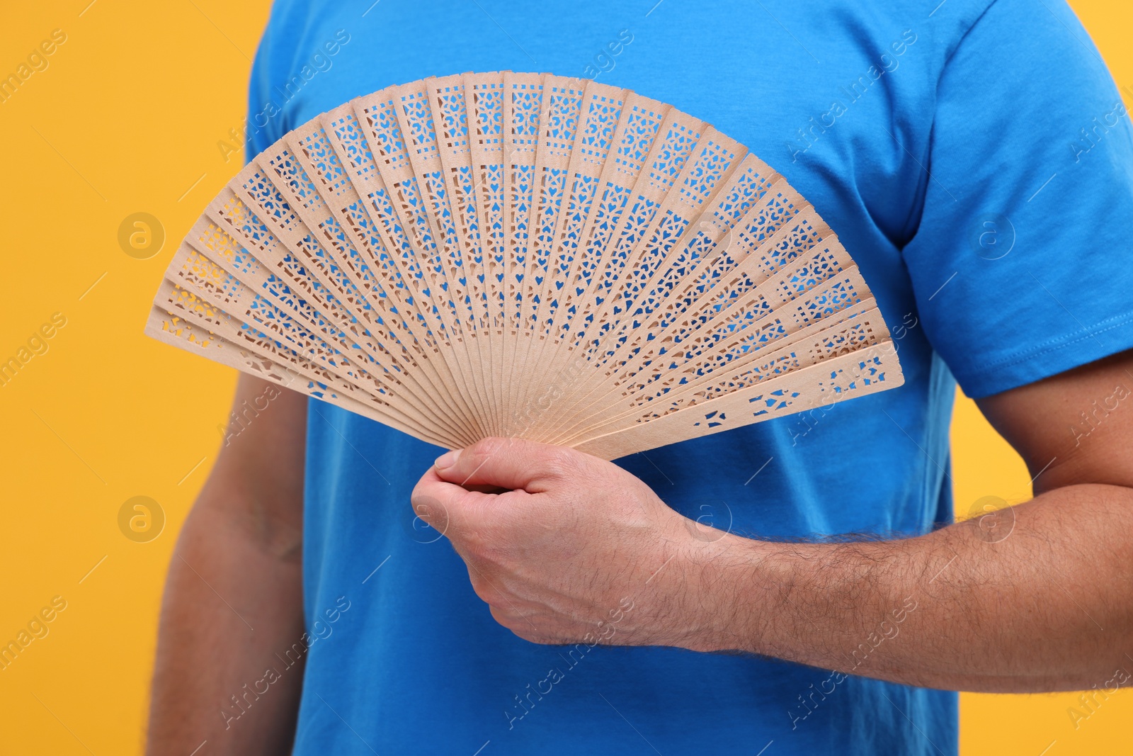 Photo of Man holding hand fan on orange background, closeup