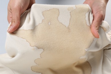 Woman holding beige sweater with stain on white background, closeup