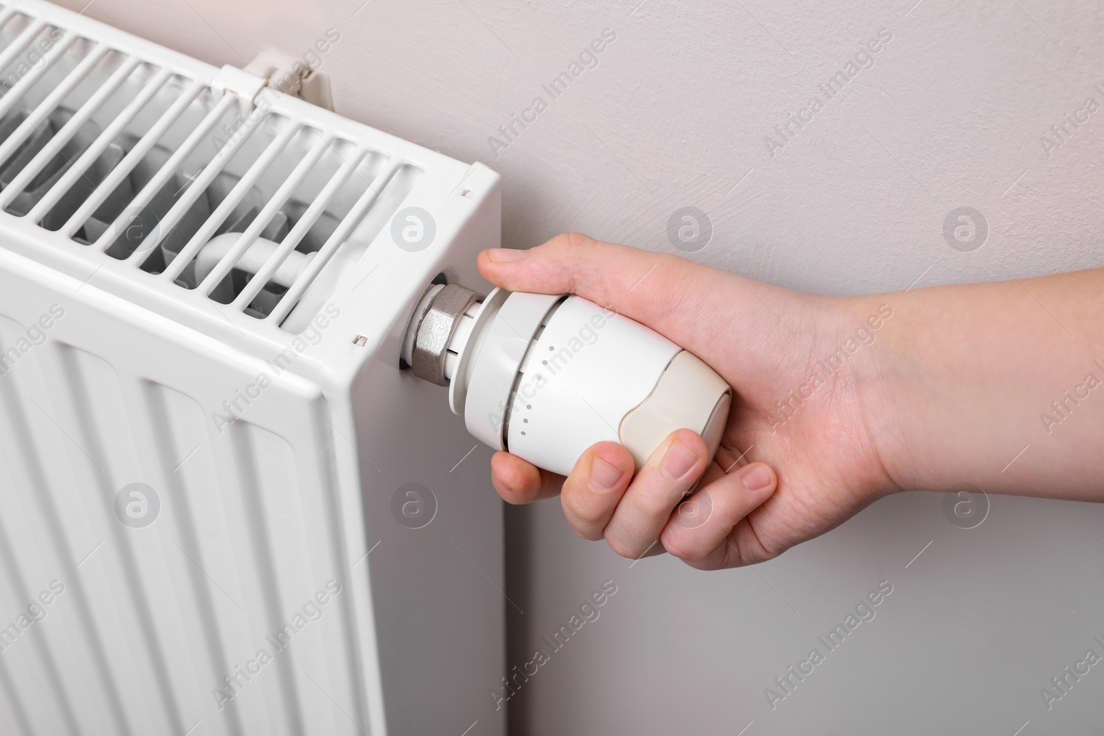 Photo of Girl adjusting heating radiator thermostat near white wall indoors, closeup