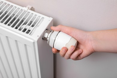 Photo of Girl adjusting heating radiator thermostat near white wall indoors, closeup