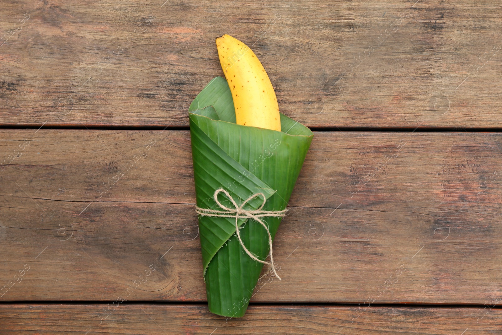 Photo of Delicious ripe banana wrapped in fresh leaf on wooden table, top view