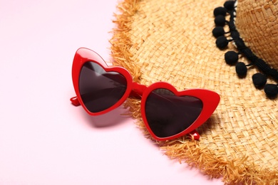 Photo of Heart shaped sunglasses and straw hat on color background, space for text