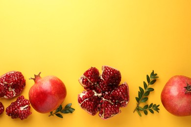 Fresh pomegranates and green leaves on yellow background, flat lay. Space for text