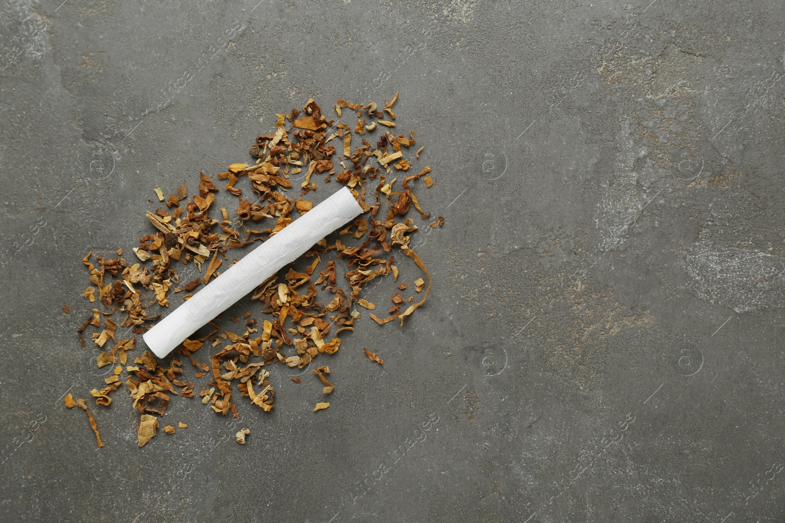 Photo of Hand rolled cigarette and tobacco on dark grey table, top view. Space for text