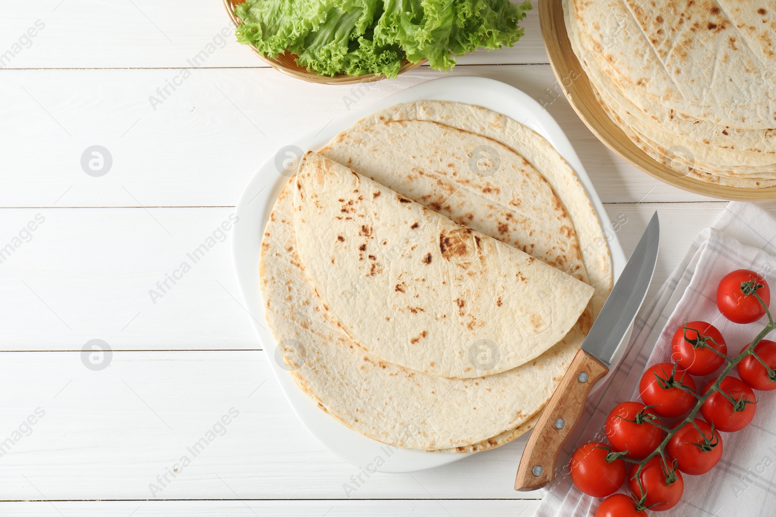 Photo of Tasty homemade tortillas, tomatoes, lettuce and knife on white wooden table, top view. Space for text