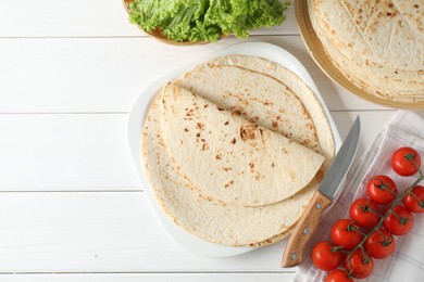 Photo of Tasty homemade tortillas, tomatoes, lettuce and knife on white wooden table, top view. Space for text