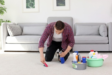 Photo of Young man cleaning carpet with brush at home