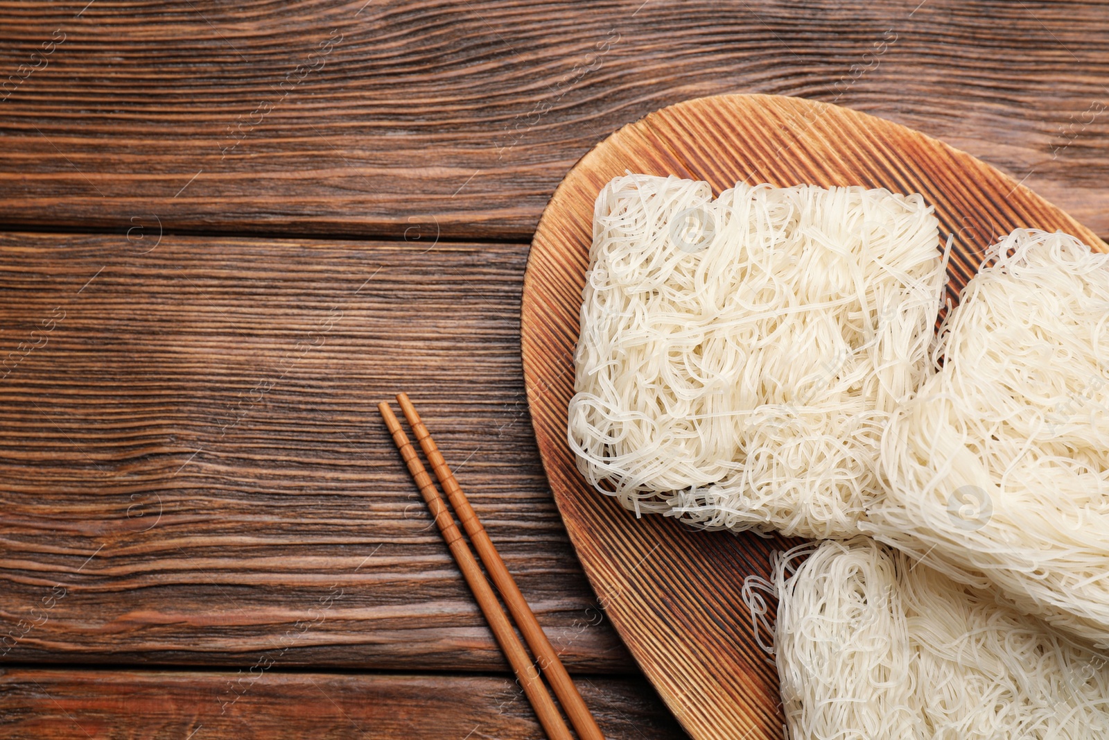 Photo of Dried rice noodles with chopsticks on wooden table, flat lay. Space for text